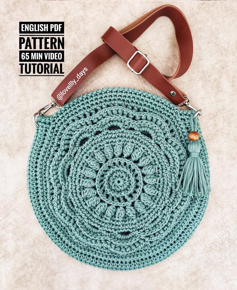 Puede incluir: Un bolso redondo de crochet de color turquesa con una correa de cuero marr&oacute;n y un borla de cuentas de madera. El bolso tiene un patr&oacute;n circular con m&uacute;ltiples capas de puntadas de crochet. El texto "ENGLISH PDF PATTERN 65 MIN VIDEO TUTORIAL @lovelily_days" es visible en la correa.