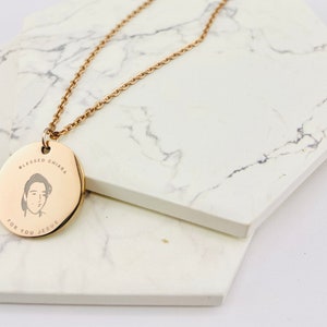 Könnte beinhalten: Eine goldene Halskette mit einem runden Anhänger, der ein Porträt einer Person mit dem Text "Blessed Chiara For You Jesus" zeigt.