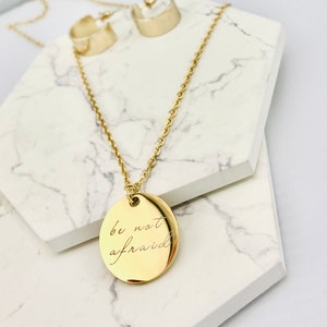 May include: Gold necklace with a round pendant that says "be not afraid" in cursive script.