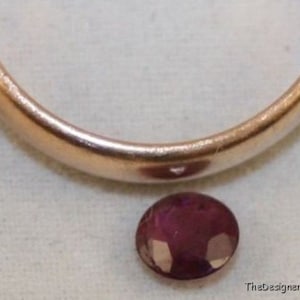 May include: A close-up of a round, purple gemstone. The gemstone is smooth and shiny, with a slight sparkle.