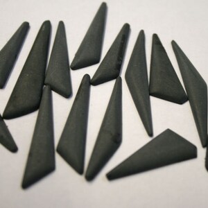 Pode incluir: Uma coleção de 15 azulejos de cerâmica de forma triangular preta. Os azulejos medem aproximadamente 3,8 cm de comprimento e têm um acabamento fosco.
