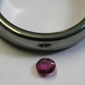 May include: A small, round, pink gemstone with a smooth, polished surface.