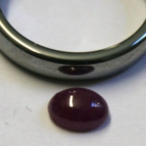 May include: A deep red cabochon gemstone, likely ruby, set in a silver ring setting.