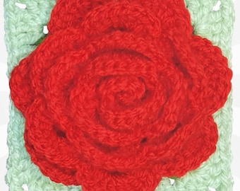 May include: A crocheted square featuring a red rose with a green border. The rose is made with a spiral pattern and has a textured appearance.