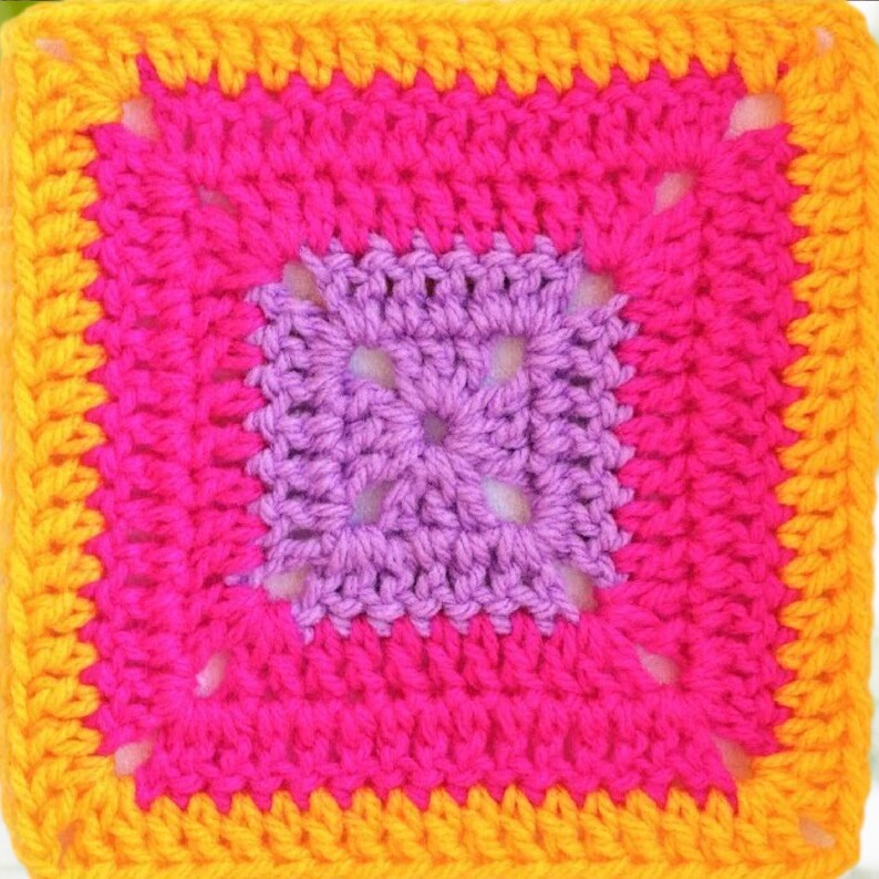 May include: A crocheted square with a purple center, surrounded by a pink border and a yellow border.