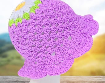 May include: A handmade crochet hat in a light purple color, featuring a daisy design with white, yellow, and green accents. The hat has a scalloped brim and is displayed on a white mannequin head.