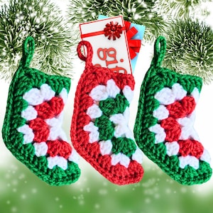 May include: Three small crocheted Christmas stockings in red, white, and green. The stockings are hanging from a Christmas tree branch.