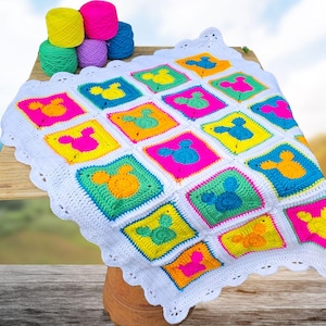 Könnte beinhalten: Eine farbenfrohe, handgehäkelte Decke mit einem sich wiederholenden Muster aus Maus-Silhouetten in leuchtenden Farben. Die Decke hat einen weißen, gewellten Rand und wird auf einer Holzoberfläche präsentiert. Garnknäuel sind ebenfalls sichtbar.