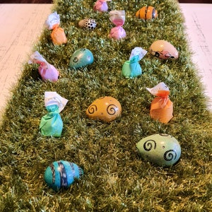 May include: Assortment of colorful Easter eggs decorated with swirls and patterns, some wrapped in foil, on a bed of sparkly green grass.