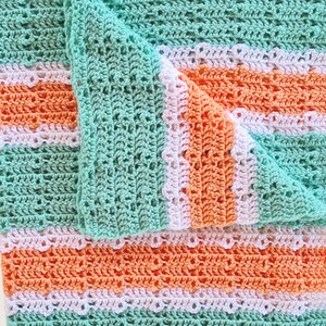 May include: A crocheted blanket with alternating stripes of light green and peach. The blanket has a white crocheted border with a scalloped edge.