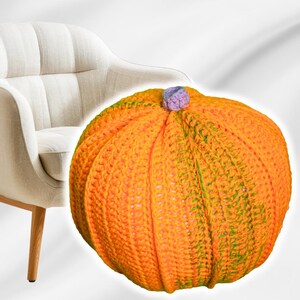 May include: A crocheted pumpkin-shaped pillow in orange and green with a purple stem. The pillow is sitting on a white surface.