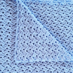 May include: A close-up of a light blue crocheted blanket with a diamond pattern. The blanket is folded in half, showing the intricate stitch work.