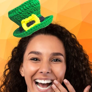 Pode incluir: Uma mulher com cabelo castanho escuro encaracolado está usando um chapéu de duende verde de crochê com uma fivela amarela e preta. Ela está sorrindo e rindo com a mão na boca.