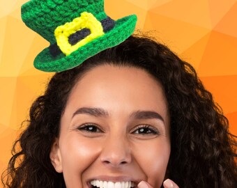 May include: A woman with curly dark brown hair is wearing a green crocheted leprechaun hat with a yellow and black buckle. She is smiling and laughing with her hand covering her mouth.