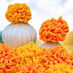 Può includere: Due oggetti decorativi bianchi e scanalati sormontati da fiori all'uncinetto arancioni brillanti. I fiori sono di un vibrante colore arancione. Una ghirlanda di fiori all'uncinetto arancioni simili è in primo piano. Lo sfondo è un cielo morbido e sfocato.