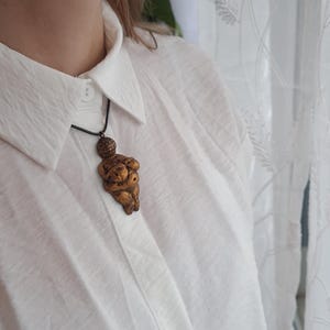 Puede incluir: Un collar dorado con un colgante con forma de cuerpo de mujer. El colgante est&aacute; detallado con una superficie texturizada y una peque&ntilde;a cabeza.