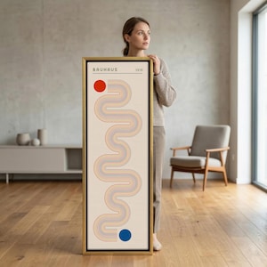 May include: A tall, rectangular framed wall art piece featuring a cream background with a vertical, winding, multi-coloured line pattern. The design includes a solid red circle at the top left, a solid blue circle at the bottom right, and the text BAUHAUS 1919.