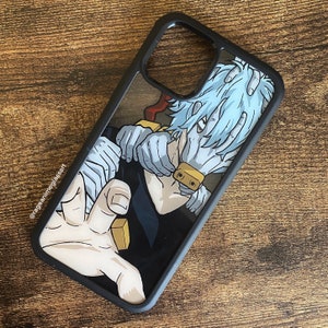 Peut inclure: Coque de t&eacute;l&eacute;phone noire avec une illustration de style anime. Le design pr&eacute;sente un personnage aux cheveux bleu clair, les mains band&eacute;es et un prot&egrave;ge-visage dor&eacute;. L'&eacute;tui a un bord noir et un dos transparent, affichant l'&oelig;uvre.