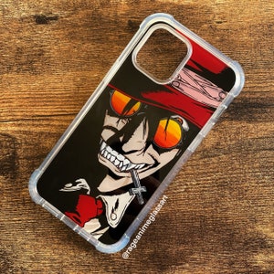 Peut inclure: Coque de t&eacute;l&eacute;phone transparente avec un personnage d'anime stylis&eacute;, portant des lunettes de soleil orange, un chapeau rouge et un pendentif en forme de croix. L'illustration est sur fond noir. La coque a un pare-chocs de protection.
