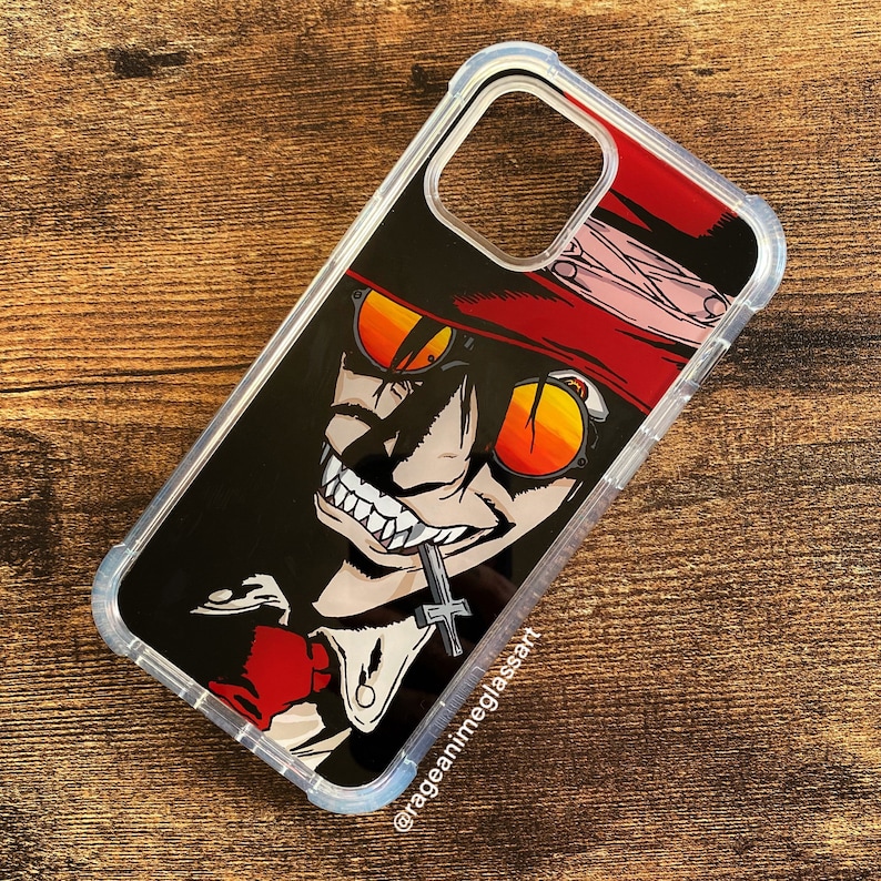 Peut inclure: Coque de t&eacute;l&eacute;phone transparente avec un personnage d'anime stylis&eacute;, portant des lunettes de soleil orange, un chapeau rouge et un pendentif en forme de croix. L'illustration est sur fond noir. La coque a un pare-chocs de protection.