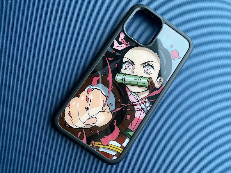 Peut inclure: Coque de t&eacute;l&eacute;phone noire avec une illustration color&eacute;e d'un personnage d'anime. Le design pr&eacute;sente un personnage aux yeux roses, une museli&egrave;re en bambou et une pose dynamique avec un poing serr&eacute;. La coque a une bordure noire.