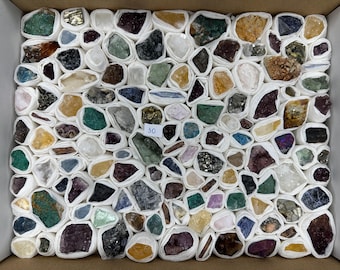 May include: A collection of assorted raw mineral stones and crystals, each individually wrapped in white paper, arranged in a grid within a cardboard box. A small white square label with the number 30 is placed near the centre of the display.