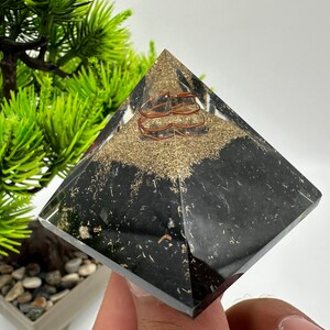 May include: Black obsidian pyramid with copper wire wrapped around the inside. The pyramid is filled with gold glitter.