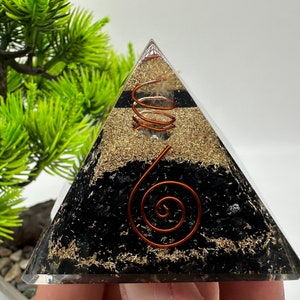May include: A clear crystal pyramid with a copper wire spiral inside. The pyramid is filled with black and gold crystals.