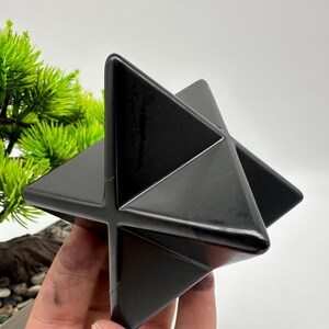 May include: A black, geometric, star-shaped crystal. The crystal is made of polished black obsidian and has a smooth, shiny surface.
