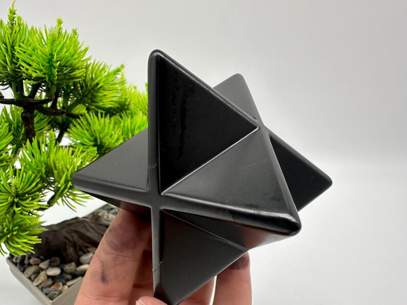 May include: A black, geometric, star-shaped crystal. The crystal is made of polished black obsidian and has a smooth, shiny surface.