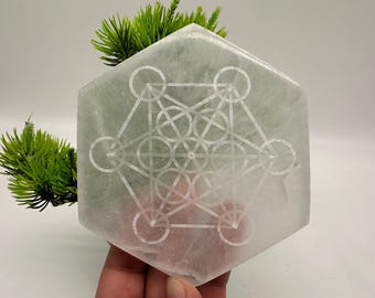 May include: A white selenite charging plate with a geometric design etched into the surface. The plate is hexagonal in shape and has a smooth, polished finish.