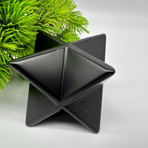 May include: A black geometric star-shaped object made of polished stone. The object is sitting on a white surface.