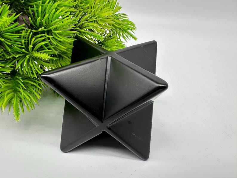 May include: A black geometric star-shaped object made of polished stone. The object is sitting on a white surface.