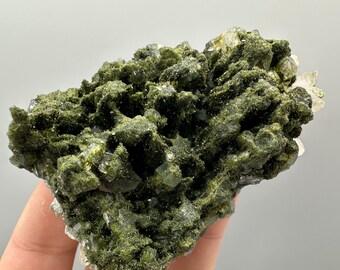 May include: A cluster of green and clear quartz crystals. The crystals are clustered together in a rough, natural formation. The green crystals are a deep, rich green, and the clear crystals are translucent.