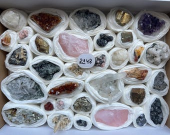 May include: A collection of various raw mineral specimens and crystals individually wrapped in white tissue paper, arranged in a rectangular box. A small white circular label with the handwritten number 2148 is placed near the centre.