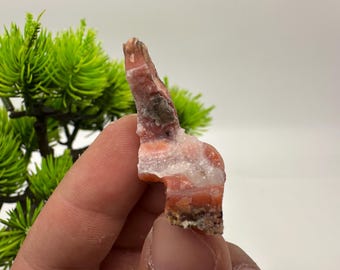 May include: A raw, natural mineral specimen with a layered appearance. The stone features bands of orange, white, and brown hues. The rough texture and unique shape suggest it is a decorative item or a collector's piece.