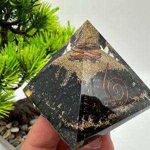 May include: Black obsidian pyramid with a copper wire spiral inside. The pyramid is clear and shows the spiral and the obsidian crystals inside.