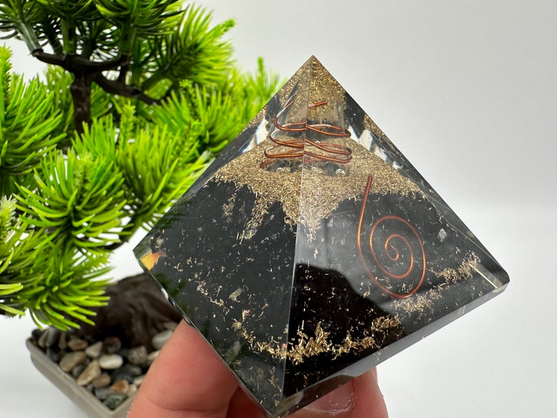 May include: Black obsidian pyramid with a copper wire spiral inside. The pyramid is clear and shows the spiral and the obsidian crystals inside.