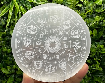 May include: White selenite charging plate with a zodiac wheel design etched into the surface. The wheel features all 12 zodiac signs, including Aries, Taurus, Gemini, Cancer, Leo, Virgo, Libra, Scorpio, Sagittarius, Capricorn, Aquarius, and Pisces.