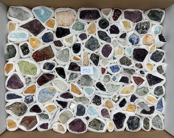 May include: A collection of assorted raw mineral specimens and crystals, each individually wrapped in white paper, arranged in a rectangular box. A small white tag with the number 133 is placed in the centre of the diverse assortment of stones.