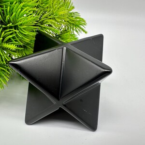 May include: A black obsidian Merkaba star, a geometric shape with six points, made of polished black obsidian.