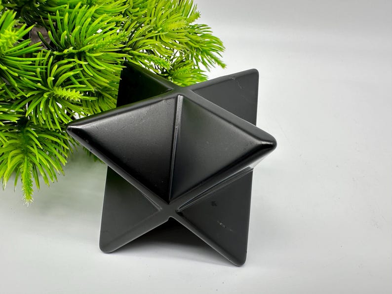 May include: A black obsidian Merkaba star, a geometric shape with six points, made of polished black obsidian.