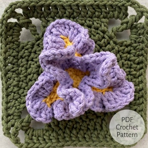 Può includere: Un motivo a fiore all'uncinetto in tonalità di viola e giallo, con un quadrato all'uncinetto verde sullo sfondo. L'immagine include il testo "PDF Crochet Pattern".