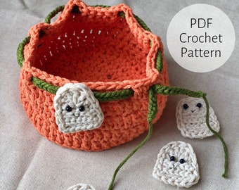 Può includere: Un cesto di zucca arancione all'uncinetto con bordi verdi e decorazioni di fantasmi bianchi all'uncinetto. Il testo "PDF Crochet Pattern" è visibile nell'angolo in alto a destra dell'immagine.