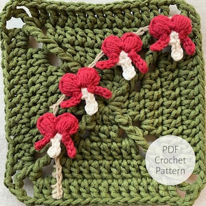 Może przedstawiać: Kwadrat wykonany na szydełku z zielonym tłem i rzędem czerwonych kwiatów z białymi środkami. Tekst "PDF Crochet Pattern" znajduje się w białym kółku w prawym dolnym rogu kwadratu.
