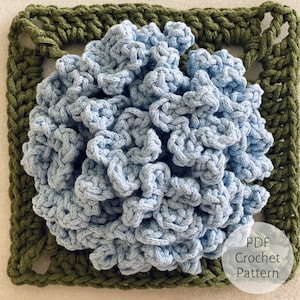 Könnte beinhalten: Ein Häkelmuster für eine blaue Blume mit grünem Rand. Das Muster ist als PDF-Download verfügbar.