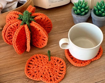 Peut inclure: Une citrouille orange crochetée avec une tige verte, un dessous de verre plat en forme de citrouille orange et une tasse en céramique blanche posée sur un second dessous de verre citrouille. Objets en fil avec mailles visibles.