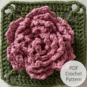 May include: A handmade crochet flower in shades of pink, centered on a green crocheted square. The flower has detailed, textured petals. The image includes a white circle with the text "PDF Crochet Pattern".