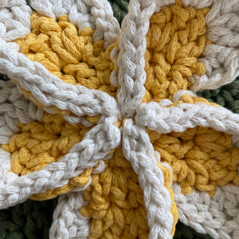 May include: Close-up of a crocheted flower with a yellow and white color scheme. The flower is made with a thick yarn and has a textured surface.