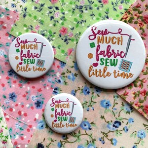 Pode incluir: Três botões redondos brancos com um design rosa, verde e laranja. Os botões têm o texto "Sew much fabric sew little time".